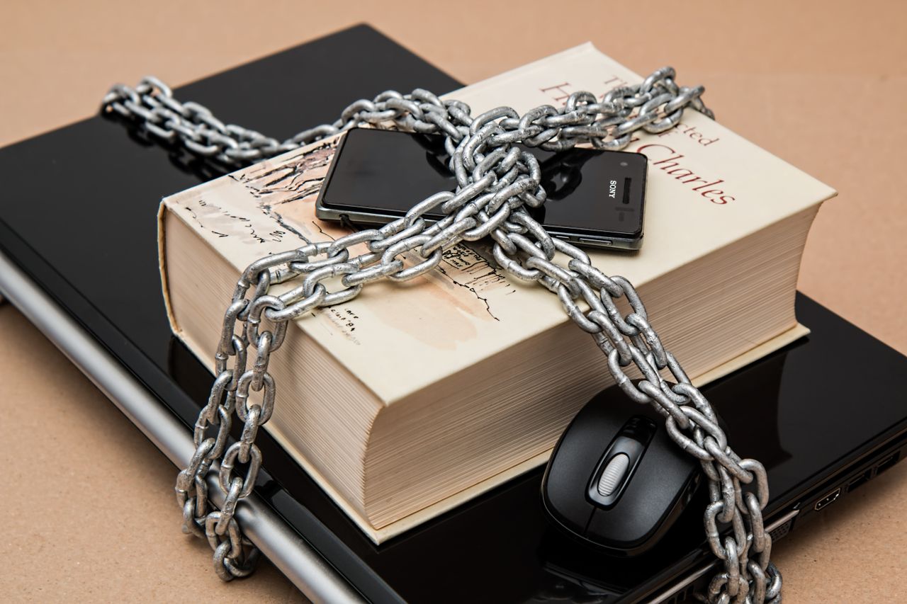 Home Chain-locked book, phone, and laptop symbolizing digital and intellectual security.